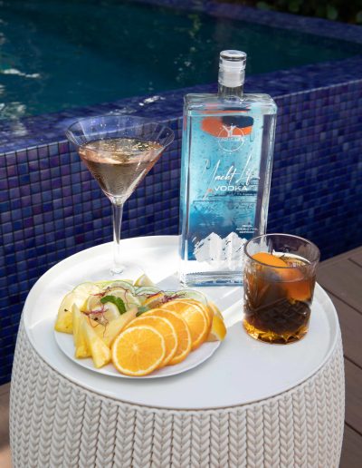 Yacht Life Vodka bottle on edge of a pool with two drinks in front of it.