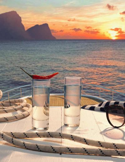 Two vodka shot glasses, one with a pepper laying on top of it. Served on top of a table with a rope and sunglasses, on the top level of a mega yacht.