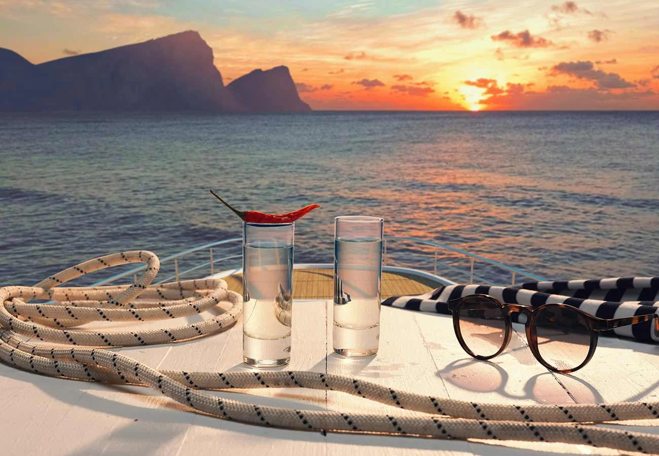 Two vodka shot glasses, one with a pepper laying on top of it. Served on top of a table with a rope and sunglasses, on the top level of a mega yacht.