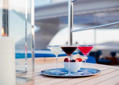 Three different fruity martini drinks on a silver tray with a bowl of cut berries.