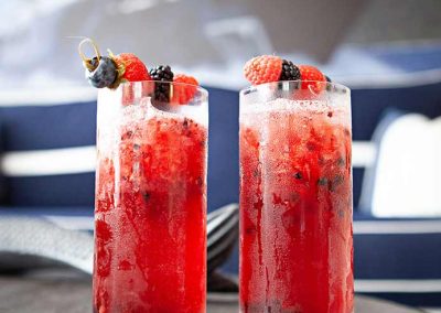 Two fruity Yacht Life Vodka cocktails on a silver tray, on a table with a painting of a yacht in the background.