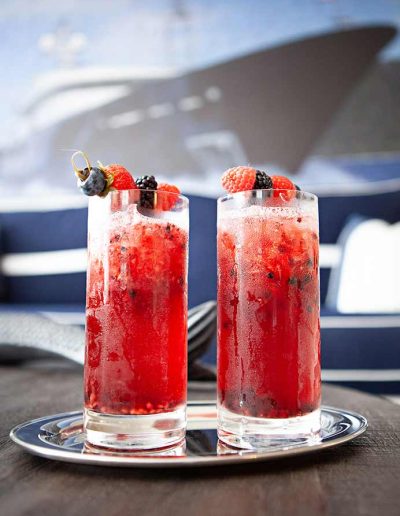 Two fruity Yacht Life Vodka cocktails on a silver tray, on a table with a painting of a yacht in the background.