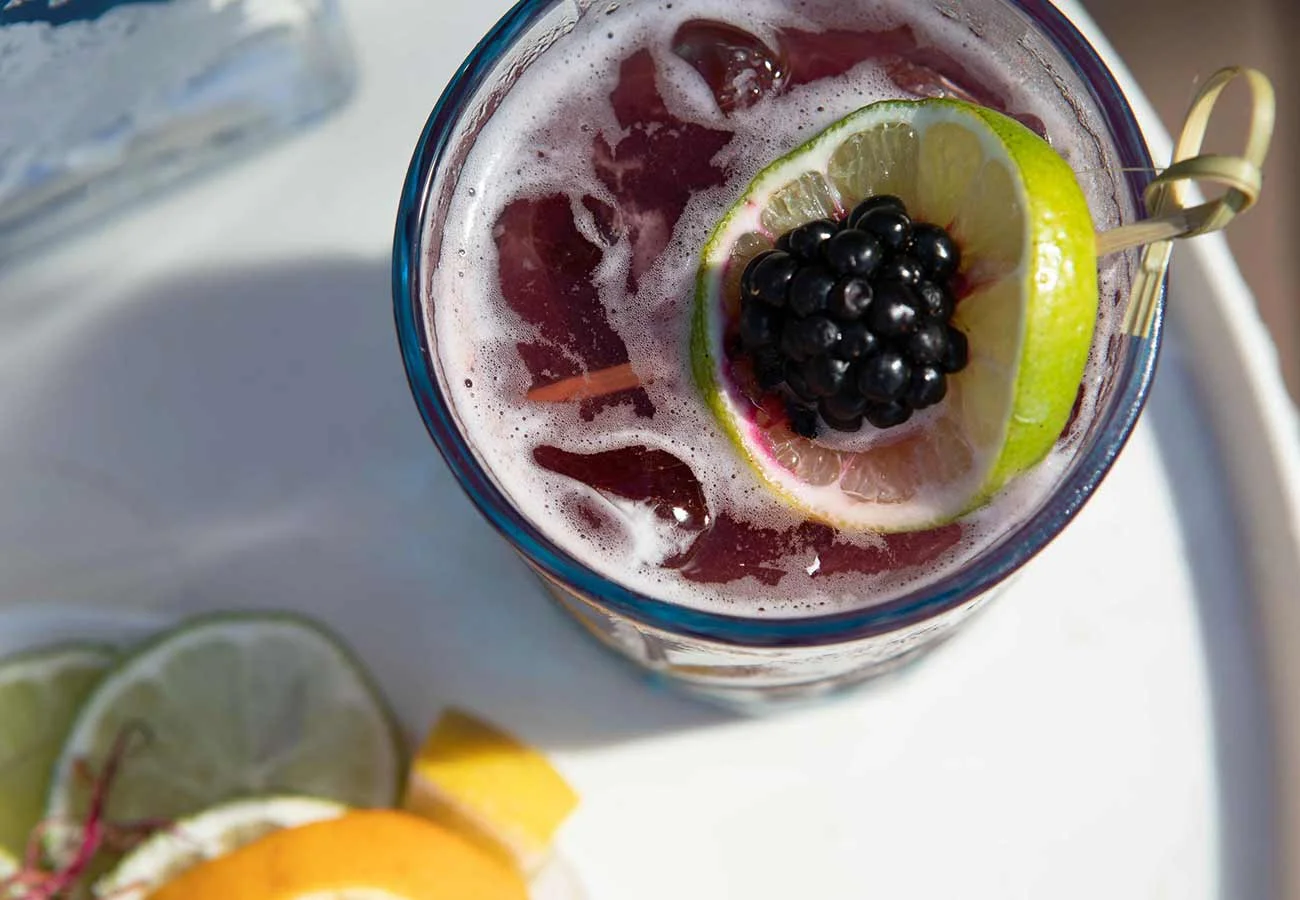 Top view of a mixed blackberry and vodka drink, garnished with a slice of lime and a blackberry.