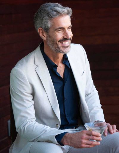 Man sitting and smiling with a martini in his right hand.